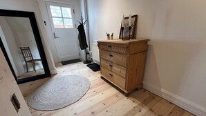 Ein Flur mit Holzboden, einem Holzschrank, einem Spiegel, einer Tür mit Fenster und einem kleinen Teppich.