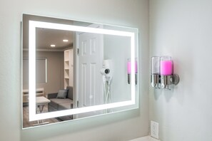 A bathroom with a large mirror, a hairdryer, and two pink soap dispensers on the wall.