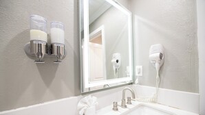Een badkamer met een wastafel, handcrème en zeepdispensers, een haardroger en een handdoek.