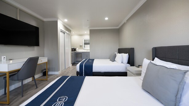 Een hotelkamer met twee bedden, een bureau, een stoel, een televisie en een kitchenette op de achtergrond.