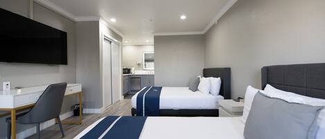 Une chambre d’hôtel avec deux lits, un bureau, une chaise, un téléviseur et, au fond, une petite cuisine.