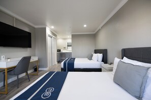 A hotel room with two beds, a desk, a chair, a TV, and a kitchenette in the background. - SGV+Disney+Rose Bowl • Quadruple Rm near DTLA (Alhambra)