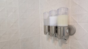 Een muurbevestigde zeepdispenser met drie transparante bakjes, elk gevuld met een andere vloeistof.