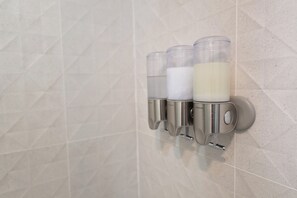 A wall-mounted soap dispenser with three transparent containers, each holding a different liquid.