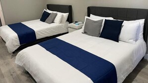 Twee bedden met wit en blauw beddengoed, een nachtkastje en een grijze hoofdbord.
