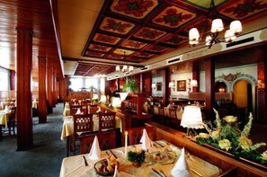Un restaurant avec des boiseries, des lustres et des tables dressées pour le service.
