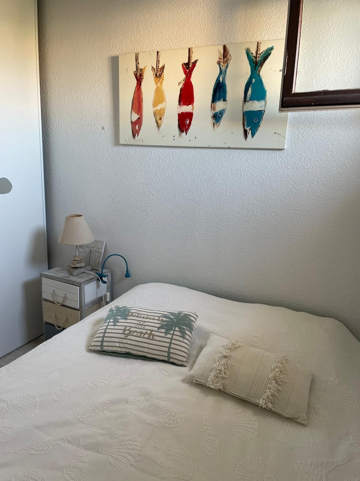 A neatly made bed with a striped pillow and a decorative pillow, a bedside table with a lamp, and a wall art piece above the bed.