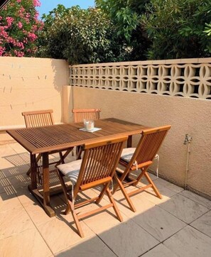 An outdoor patio with a wooden table and chairs, a white cup, and a beige wall with a decorative lattice. - Luxury 3-Bedroom Home with Large Patio Between the Ocean and the Lagoon (Le barcares)