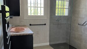 Un baño moderno con cabina de ducha de vidrio, un lavamanos y un mueble de tocador negro.