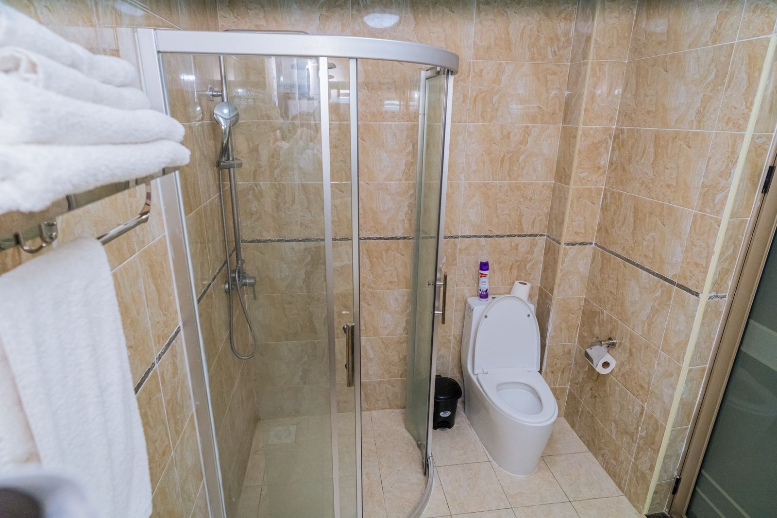 Ein Badezimmer mit einer gläsernen Duschkabine, einer Toilette und einem Handtuchhalter mit Handtüchern.