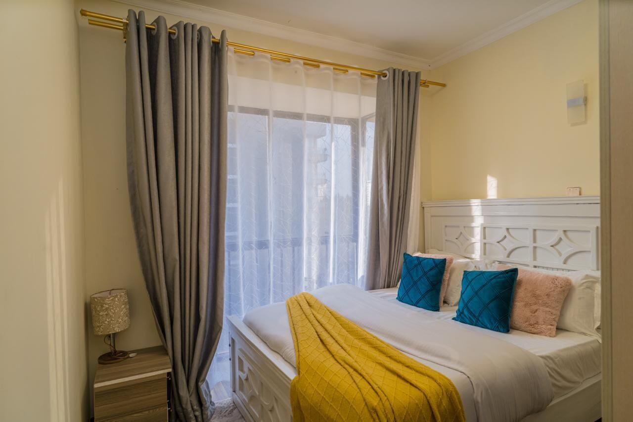 A bedroom with a bed, curtains, a bedside lamp, and a headboard.
