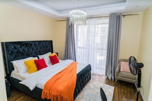 Ein Schlafzimmer mit einem großen Bett, einem Sessel, einem Ventilator und einem Fenster mit Vorhängen.