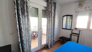A bedroom with a bed, a sliding glass door, a chair, and a small table. - Aura Conil 32326 in Conil de la Frontera (Conil de la Frontera)