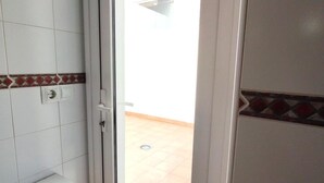 A bathroom with white tiles, a red and white patterned border, a white sink, and a door leading to a tiled floor. - Aura Conil 32326 in Conil de la Frontera (Conil de la Frontera)
