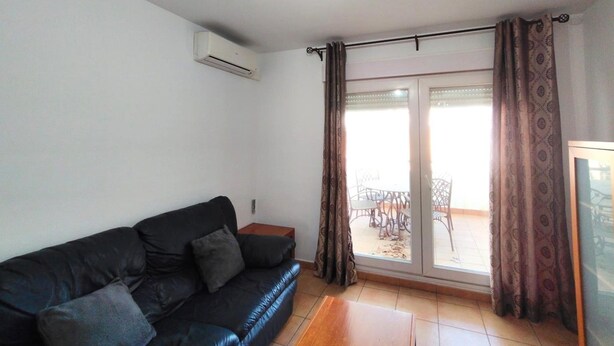 A living room with a black sofa, a small wooden table, and a sliding glass door leading to an outdoor area with chairs. - Aura Conil 32326 in Conil de la Frontera (Conil de la Frontera)