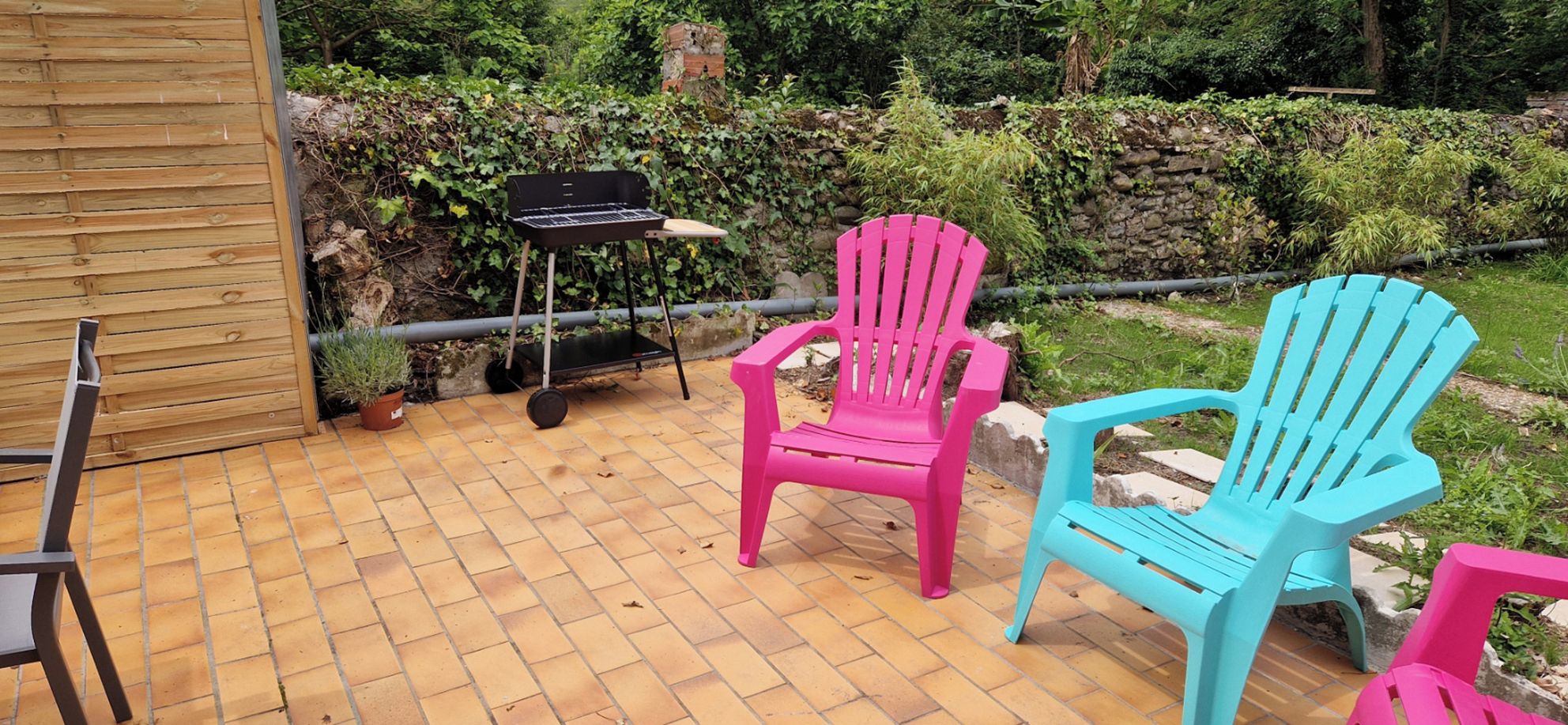 Eine Terrasse im Freien mit Terrazzo-Boden, zwei Adirondack-Stühlen, einem Grill und einem Blumentopf.