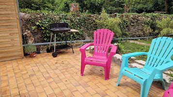 Eine Terrasse im Freien mit Terrazzo-Boden, zwei Adirondack-Stühlen, einem Grill und einem Blumentopf.