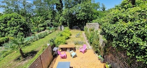 A patio area with a wooden table and two pink chairs, surrounded by lush greenery and a stone wall. - 🏡 Spacious townhouse with a garden – Sleeps up to 10 people. (Oloron-sainte-marie)