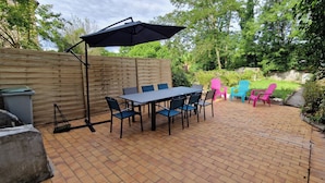 A patio with a table and chairs, a grill, and a wooden fence.