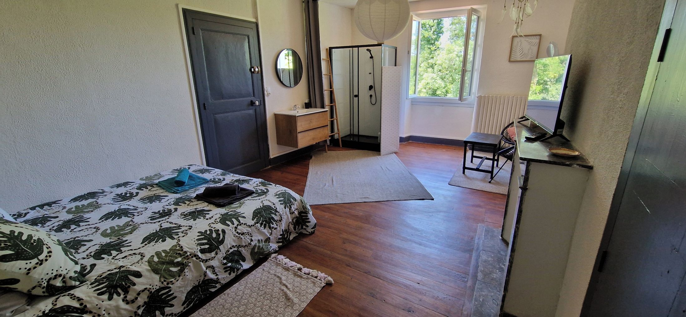 A bedroom with a bed, a dresser, a mirror, a shower, and a window.
