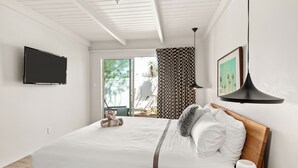Habitación de hotel moderna con una cama grande, televisor de pantalla plana, cabecera de madera, mesita de noche con una taza y vistas al exterior.