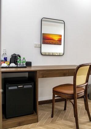A compact hotel room with a wooden desk, a compact refrigerator, a chair, and a wall-mounted picture of a sunset. - Sunset Mountain View Resort (Vang Vieng)