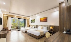 Habitación de hotel con dos camas, un escritorio, una silla, un televisor y un balcón con vistas a zonas verdes.