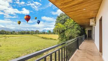 Un balcón techado con vistas a un campo verde y globos aerostáticos a lo lejos.