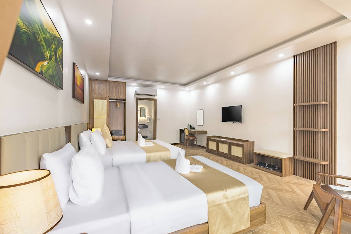 A hotel room with two beds, a desk, a TV, and a seating area.
