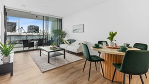 A modern living room with a dining area, large windows, and a view of the cityscape. - Walk to The Gabba | Stylish with Rooftop Views (Woolloongabba)