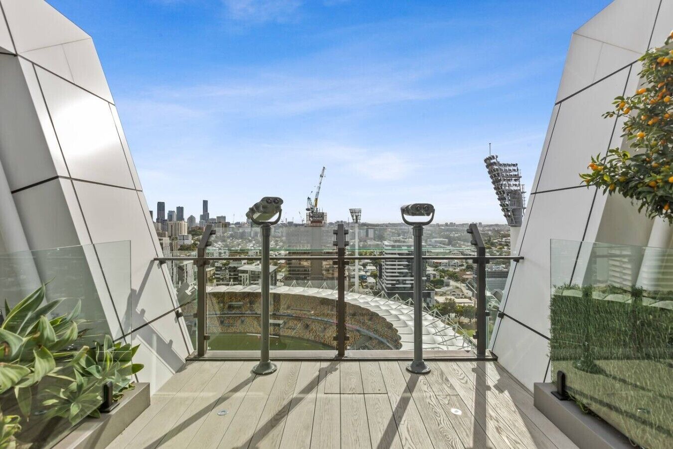 Um edifício moderno com fachada de vidro, um deck de madeira e vista para o horizonte urbano.