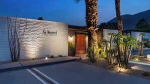 A building with a white brick facade, a wooden door, and a sign reading 'The Weekend Palm Springs.'
