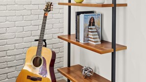 Een kamer met een witte bakstenen muur, een houten gitaar, een zwart metalen rek met decoratieve objecten en een ingelijst beeld.