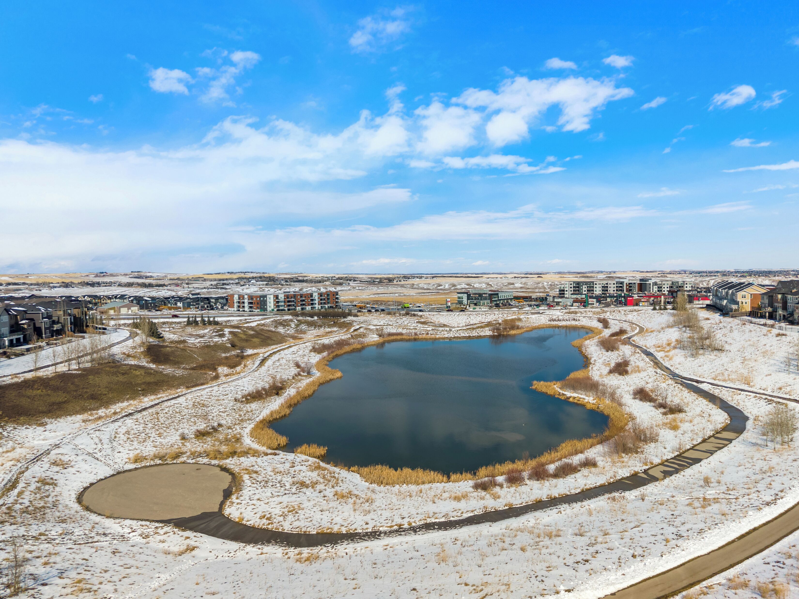A residential area with multiple apartment buildings, a large pond, and a clear sky.