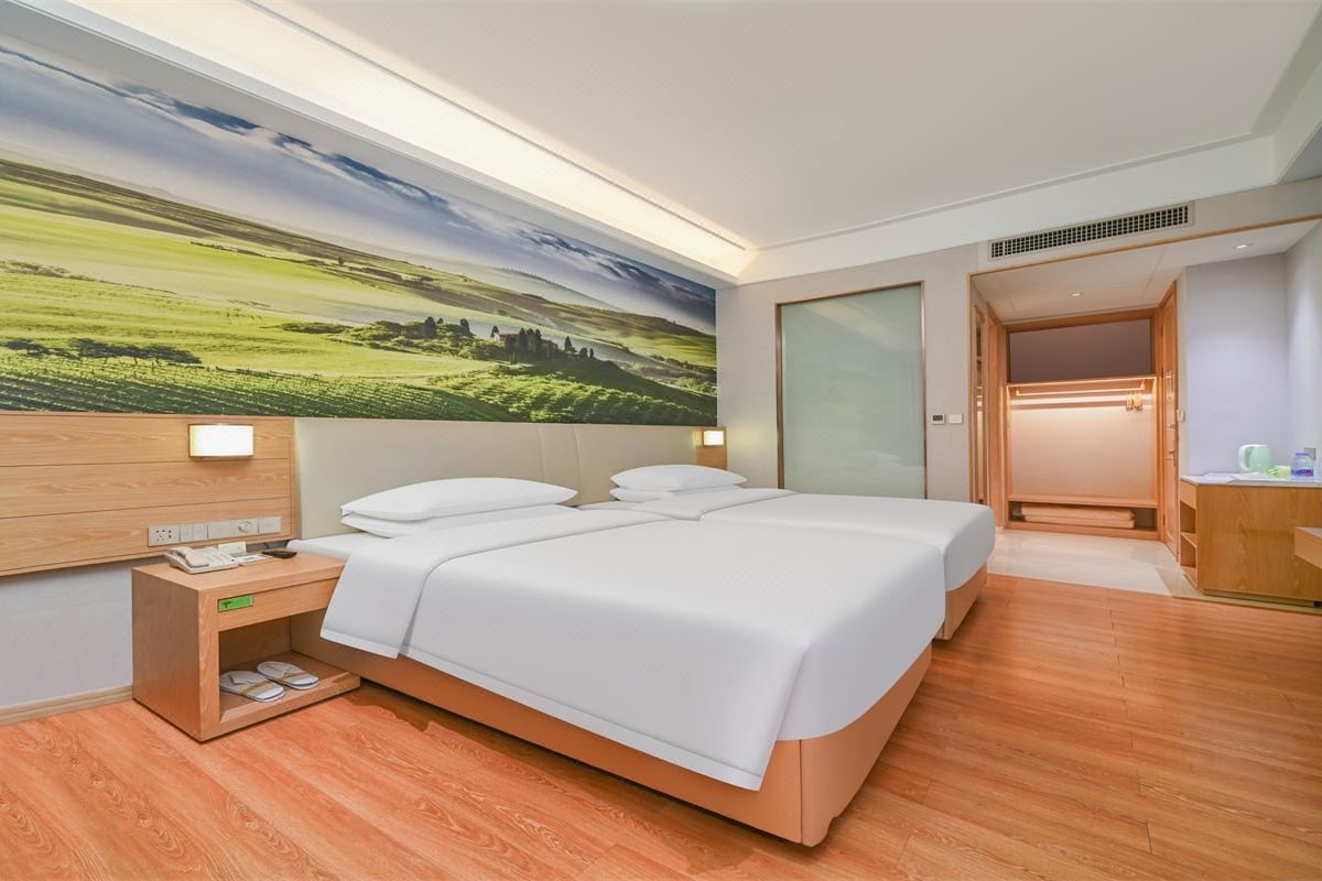 A hotel room with a large bed, a bedside table with a phone, and a wall-mounted light.