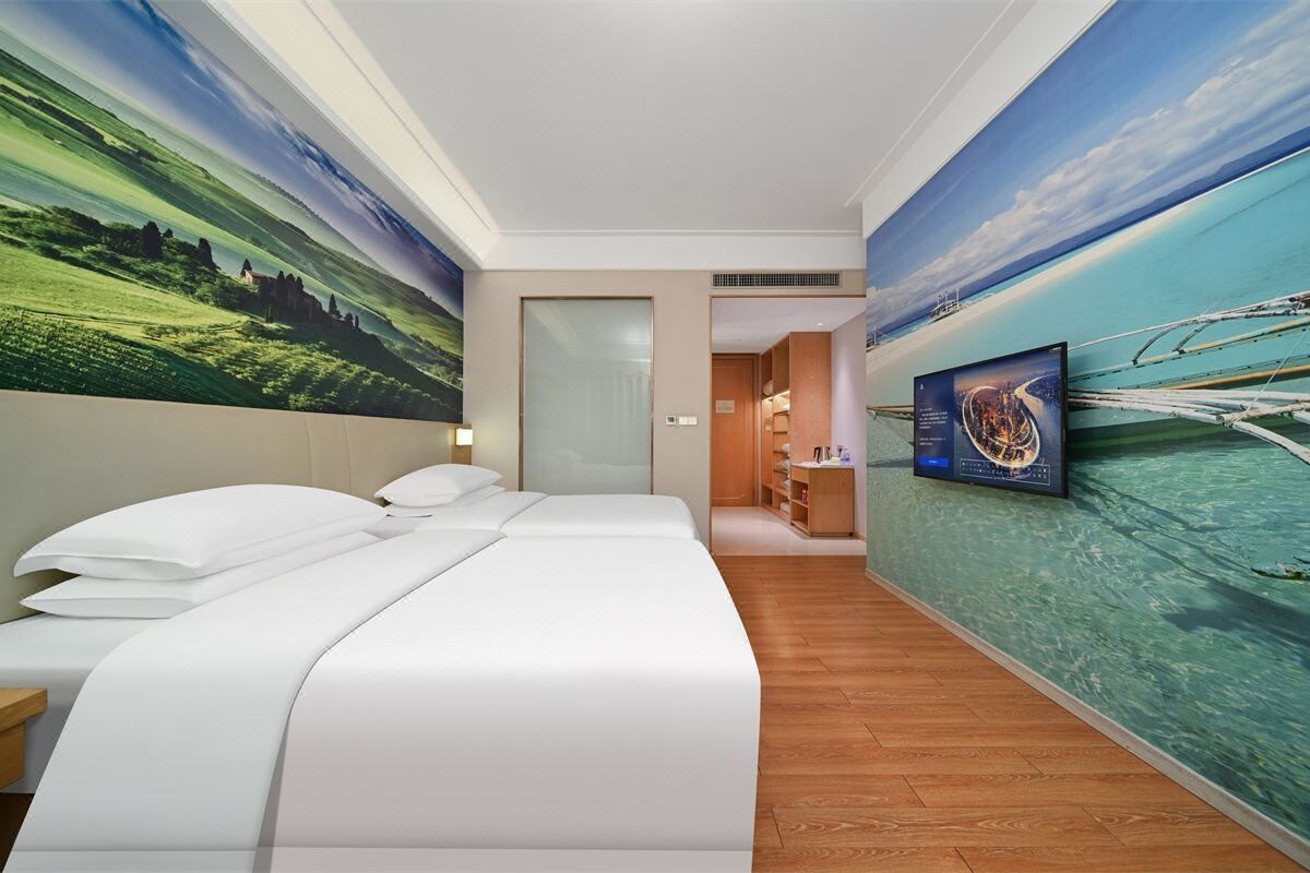 A hotel room with a large bed, a television, and a mural of a landscape.