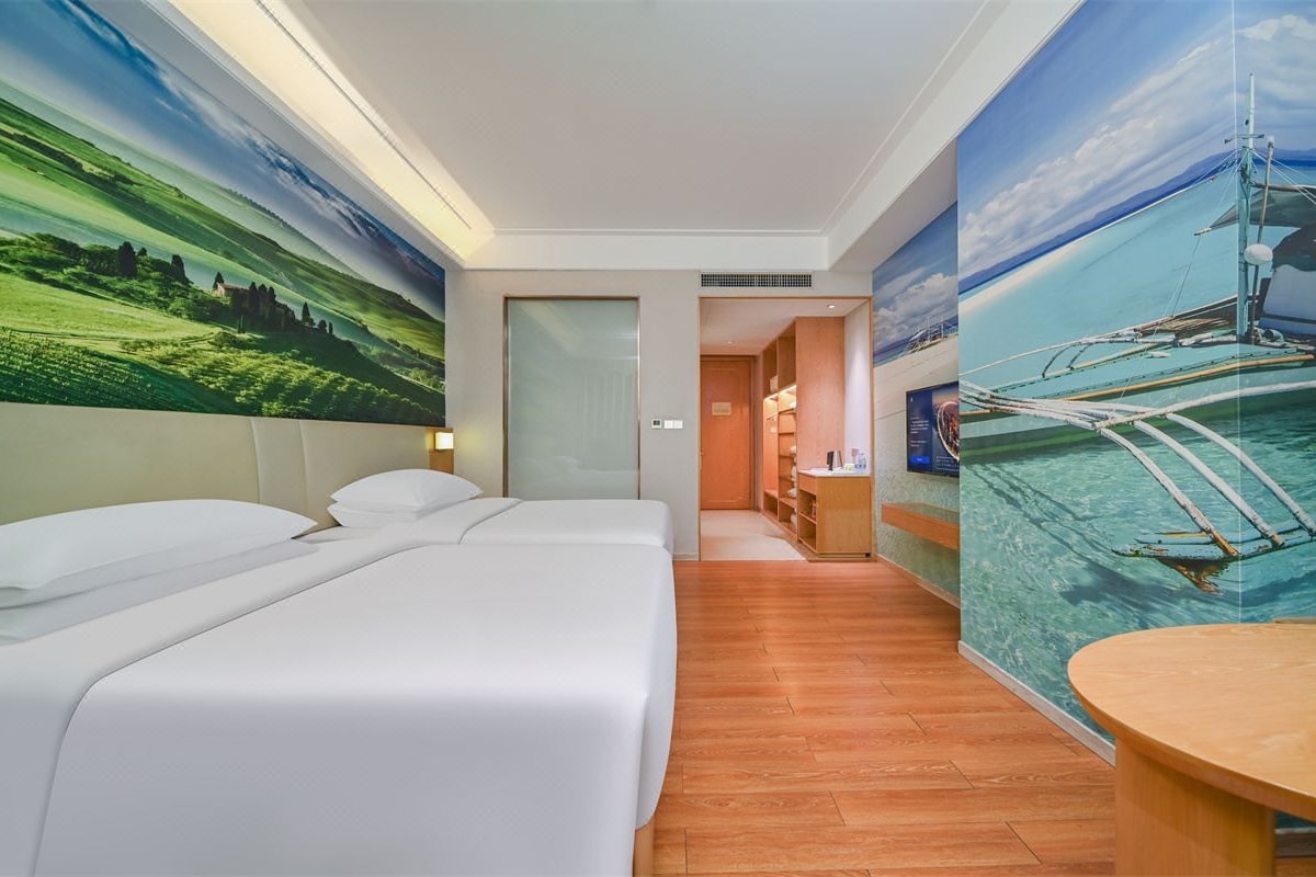 A hotel room with two beds, a wooden floor, and a large painting of a landscape and a boat on the wall.