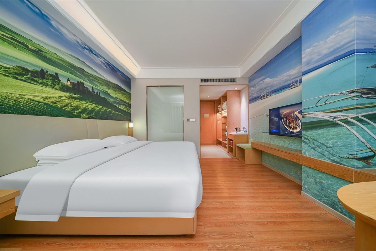 A hotel room with a large bed, a wooden floor, a bathroom with a shower, and a wall with a mural of a landscape.