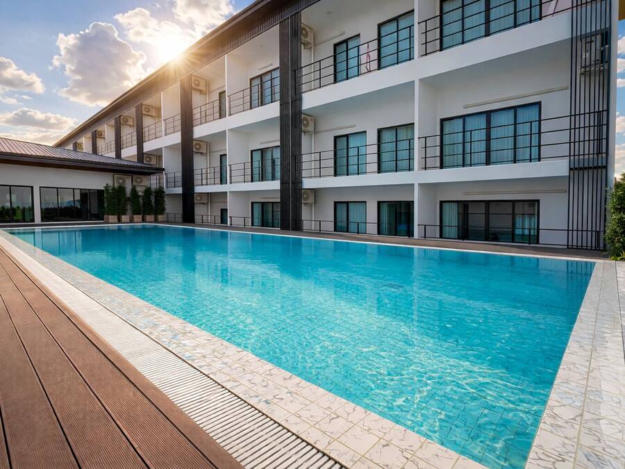 A modern hotel with a swimming pool, multiple balconies, and a clear sky.