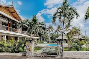 A resort with a pool, palm trees, and a thatched-roof building. - Boutik Retreats (Le Morne)