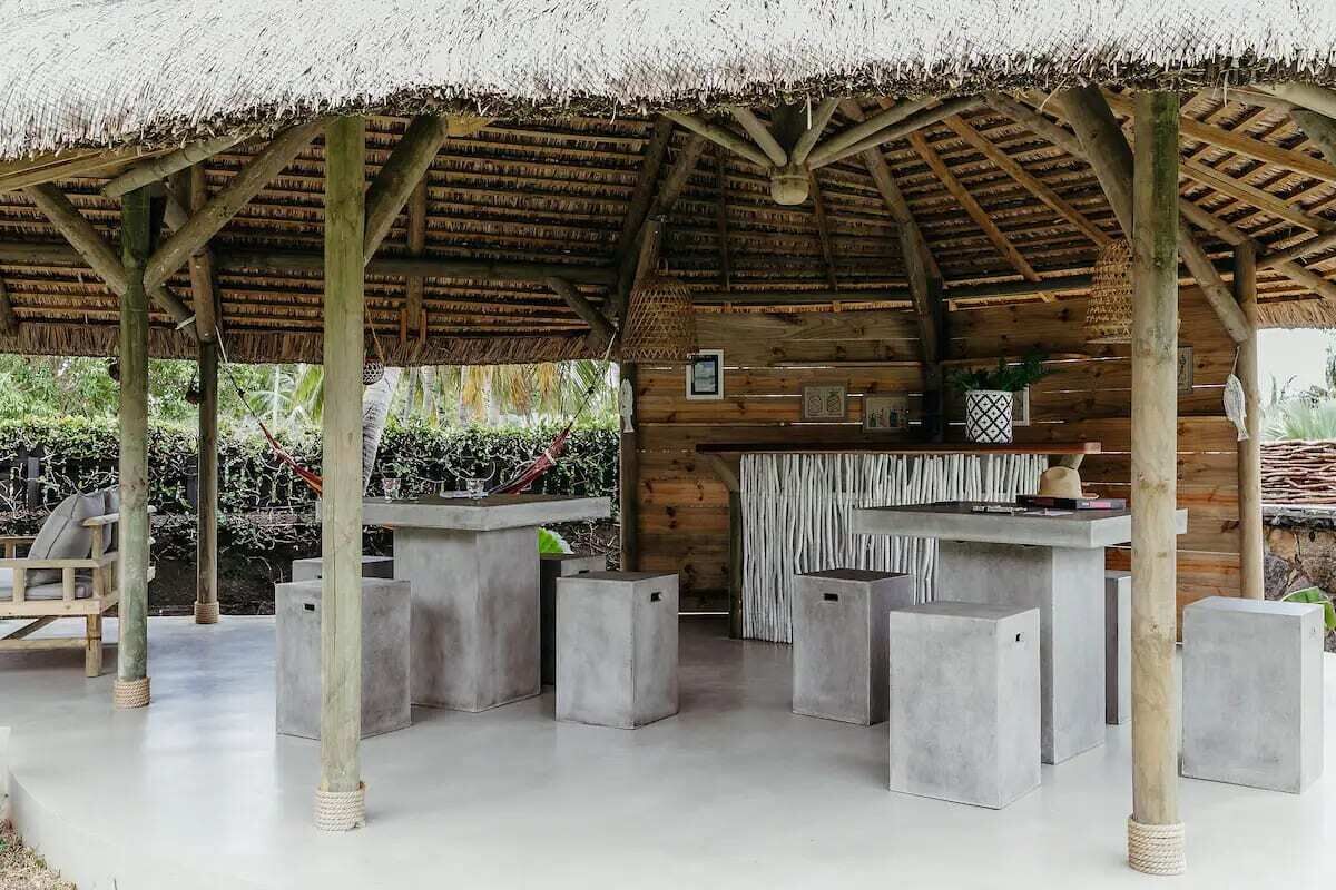 A covered outdoor area with a thatched roof, concrete seating, and wooden walls.