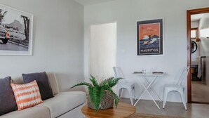 Una sala de estar con un sofá, una mesa de centro y un comedor con sillas y una mesa. Hay cuadros en la pared.