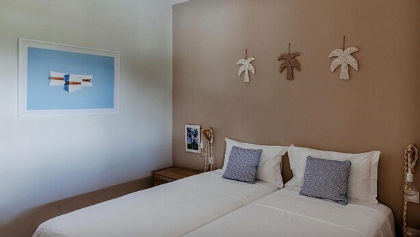 Un dormitorio con cama, almohadas, un cuadro en la pared y tres adornos de palmera.