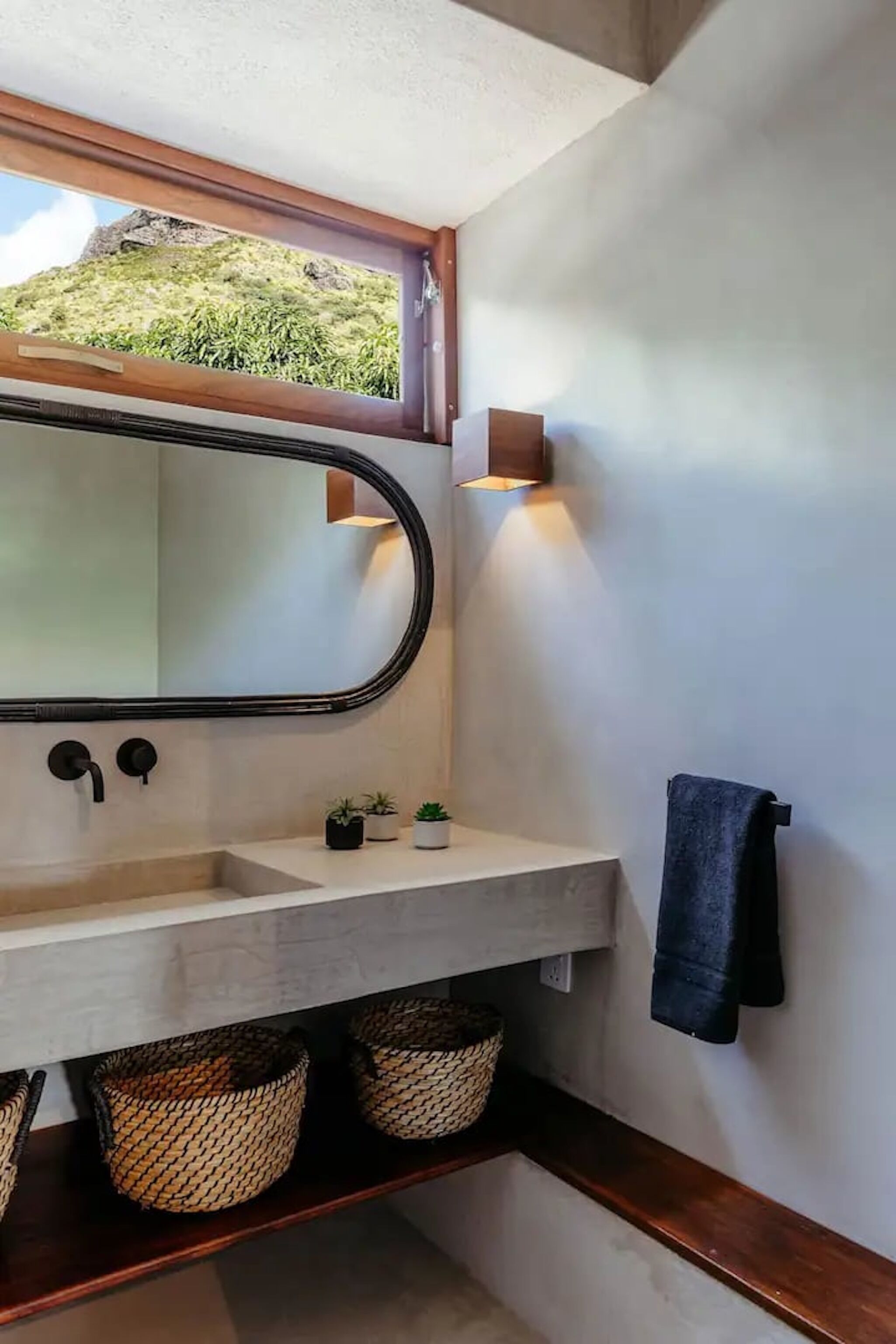 A bathroom with a large mirror, a sink, a towel rack, and a window with a view of greenery.