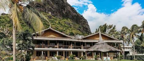 Un resort con piscina, edificaciones de techo de paja y montañas al fondo.
