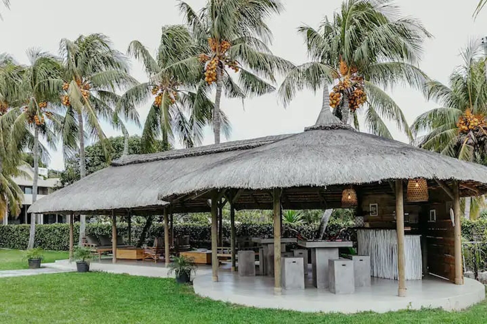 A thatched-roof pavilion with outdoor seating, surrounded by palm trees.