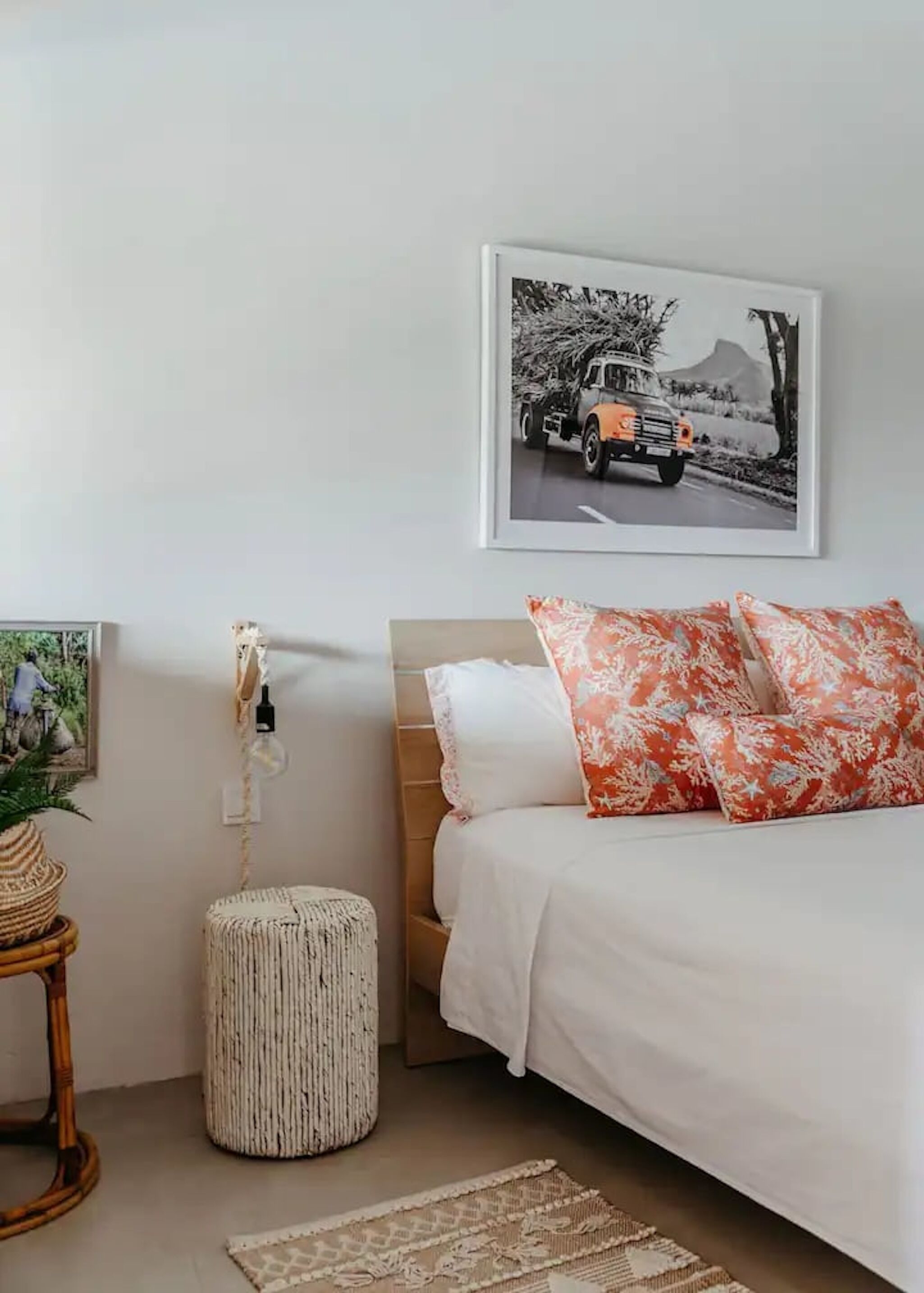 Una camera da letto con un letto, un comodino con una lampada, un quadro incorniciato appeso al muro e un pouf rotondo.