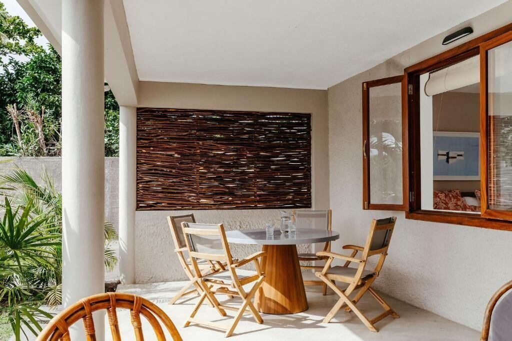 A patio with a round table and chairs, a woven wall, and a window with a view.