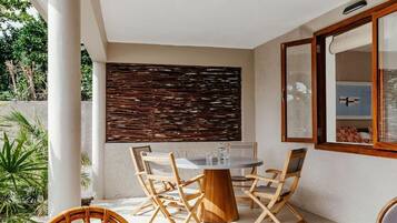 Un patio con una mesa redonda y sillas, un muro tejido y una ventana con vistas.