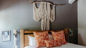 Un dormitorio con una cama, una mesita de noche, un tapiz de macramé y un cuadro en la pared.